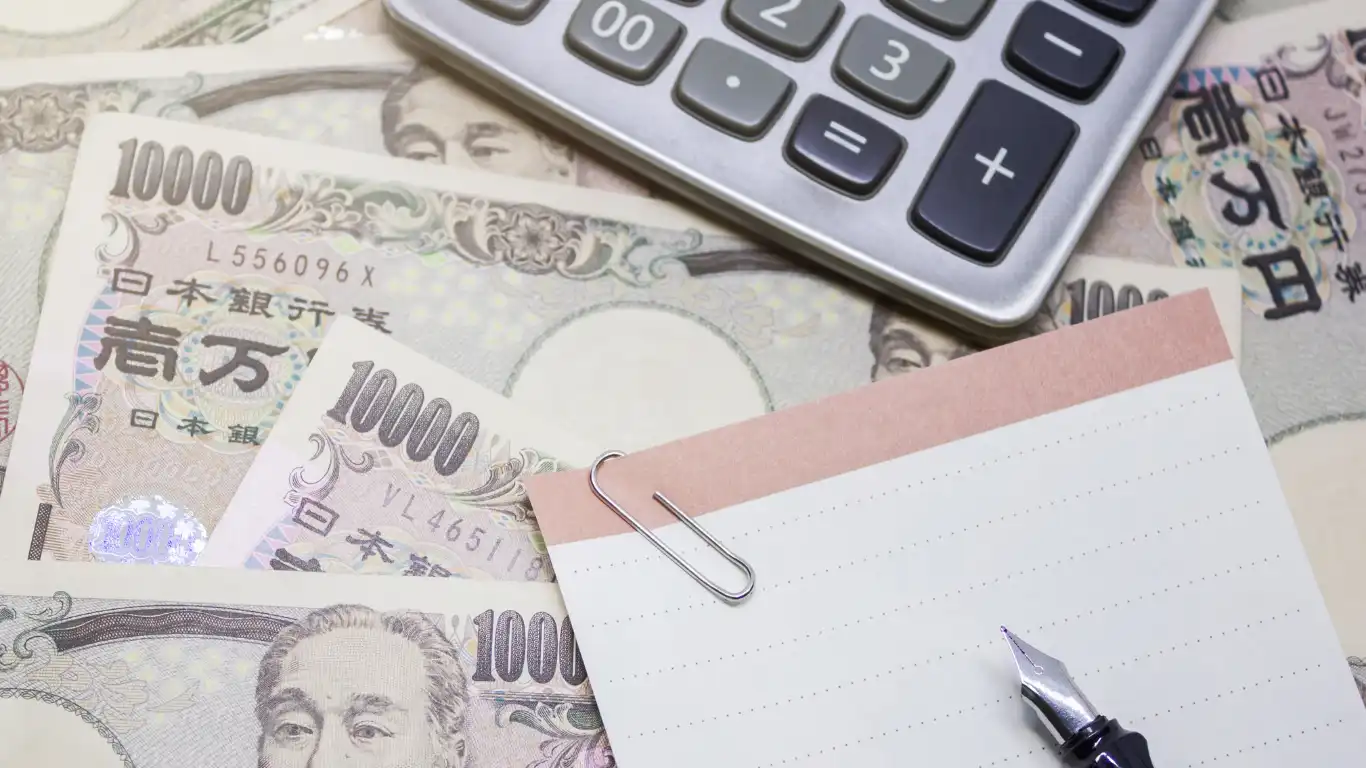 1万円札の上に置かれた電卓とメモ帳
