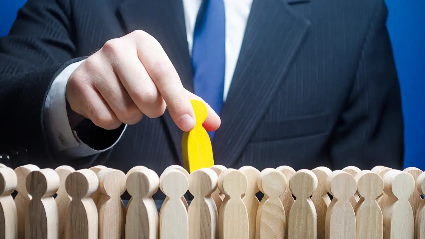 たくさんの人形から黄色の人形を選び取っているスーツ姿の男性