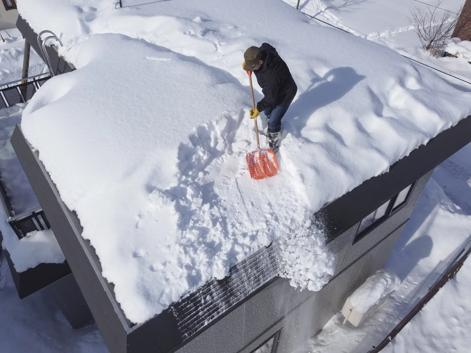 屋根に登って雪かきをしている男性