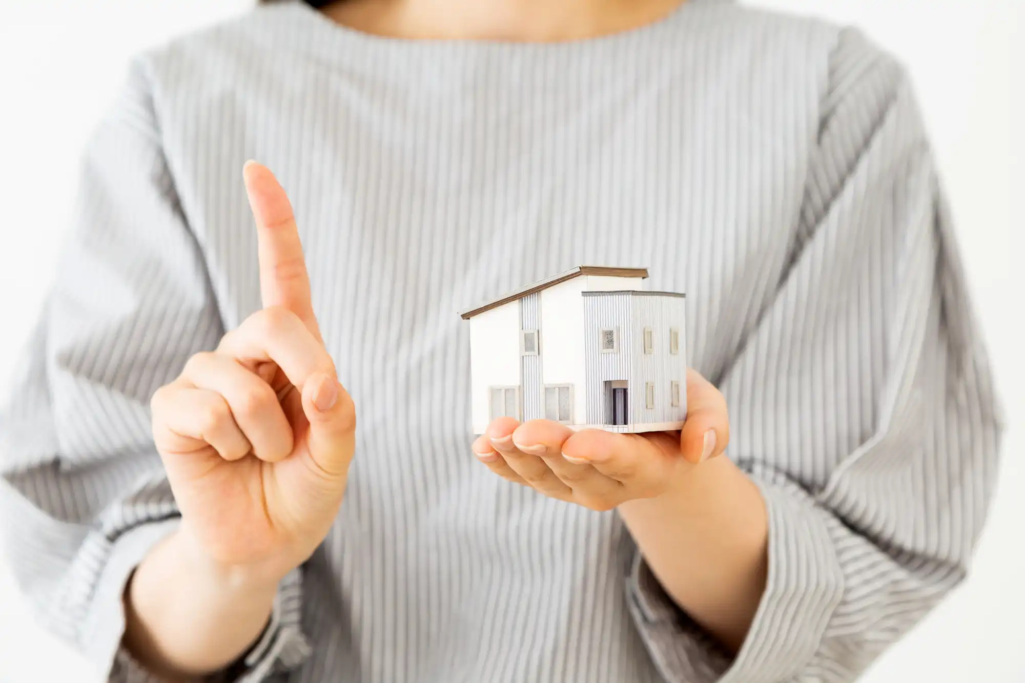 家の模型を持って、逆の手で指差しをしている女性