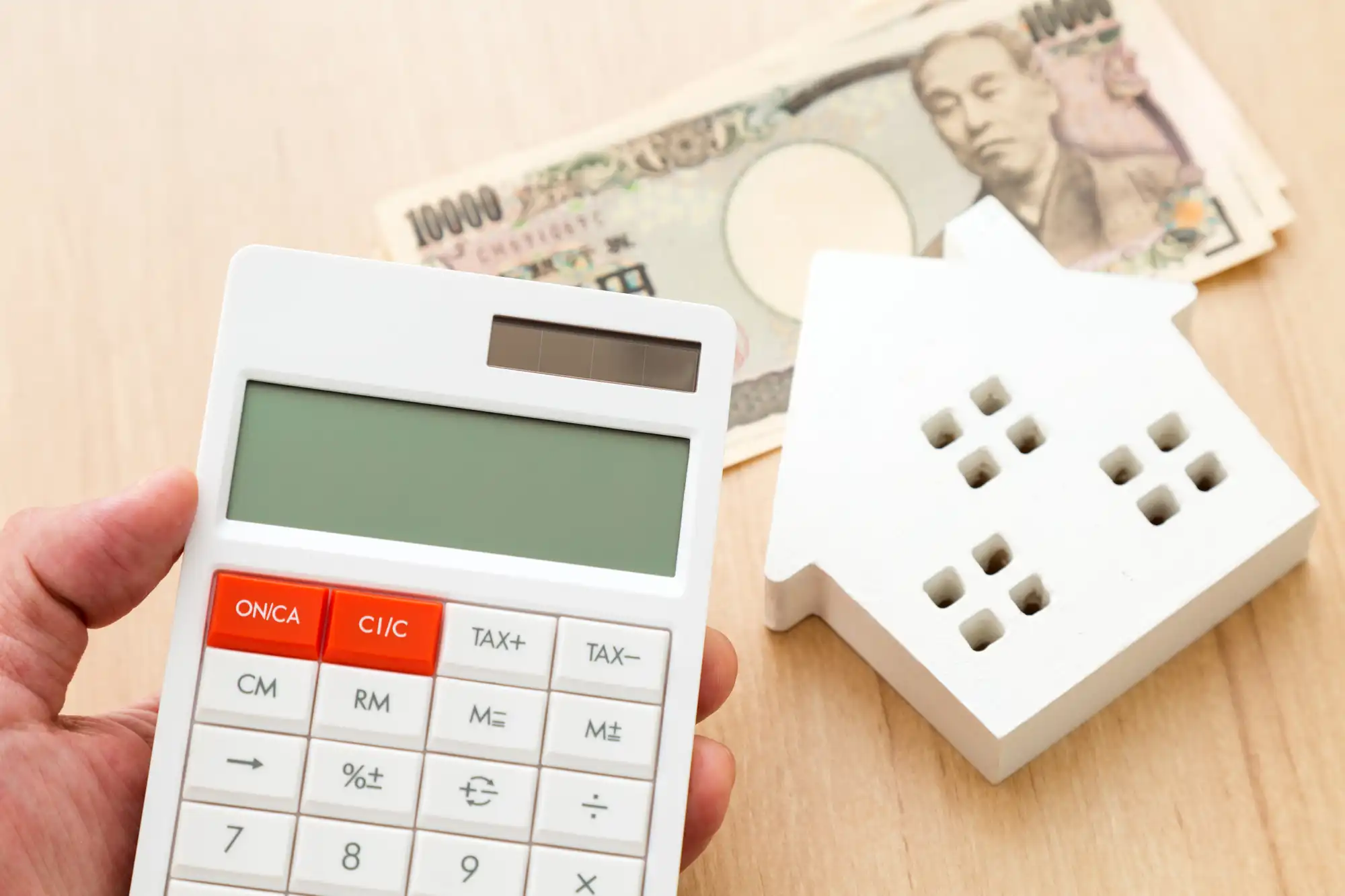 机に置かれた1万円札と家の模型を見ながら電卓を持っている